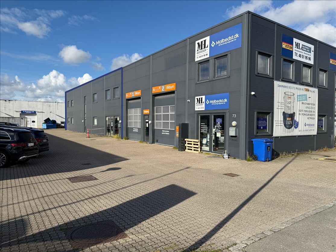 To biler parkeret foran en bygning med skilte for Mailbedst og Jotun 73 og en skraldspand med hjul uden for døren