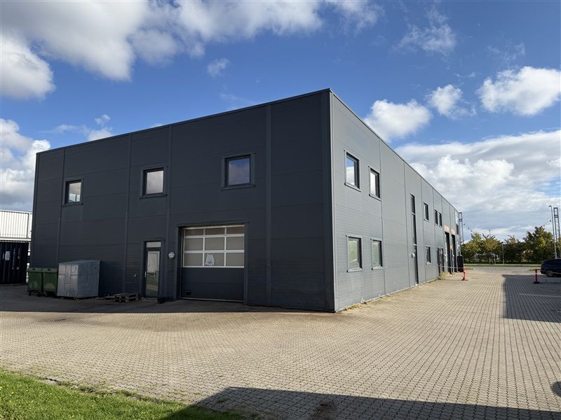 En stor sort bygning med mange vinduer og en stor garagedør i forgrunden og to røde søjler på højre side