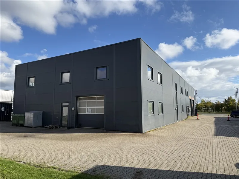 En stor sort bygning med mange vinduer og en stor garagedør i forgrunden og to røde søjler på højre side