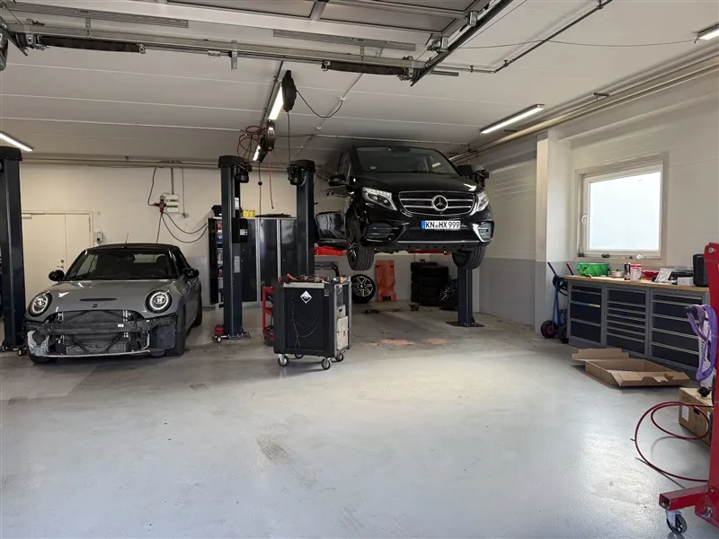 En bilværksted med to biler, en Mini Cooper og en Mercedes-Benz, samt værktøjskufferter og højtløfter
