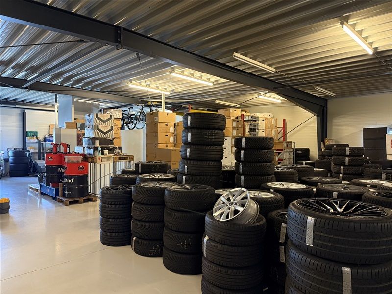 Et lager med masser af bil- og motorcykeldæk samt fælge, hvor flere dæk er sammenlagt i søjler og spredt rundt i rummet