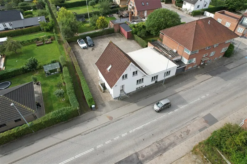 En kontorejendom med parkeringsplads på Prangervej 43 i Fredericia med to parkerede biler og en bil kører forbi på vejen