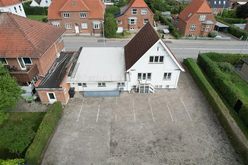 Foto viser en hvid kontorejendom med et stort parkeringsområde og flere naboer i baggrunden