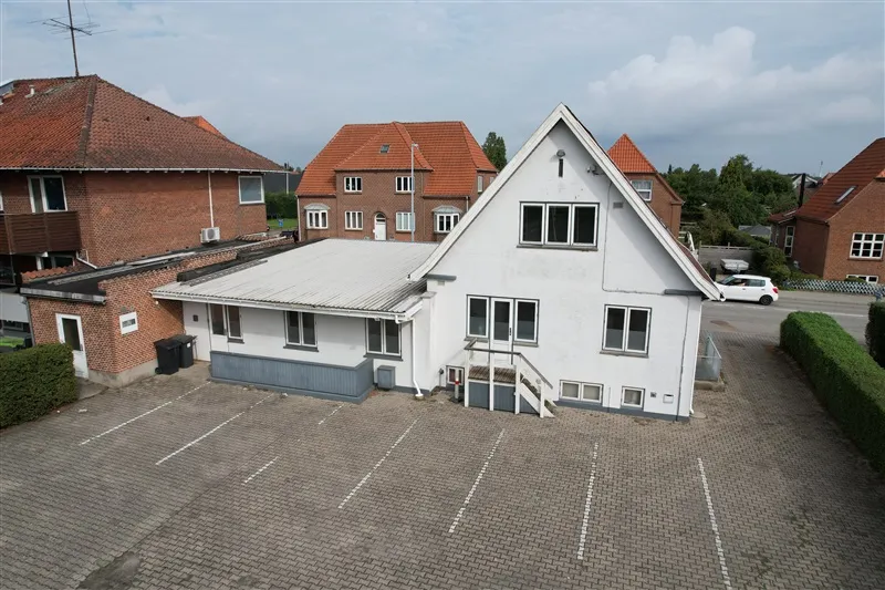 Kontorejendom med terrasse og parkeringsplads på Prangervej 43 i Fredericia. Tre bygninger i baggrunden med røde tag og