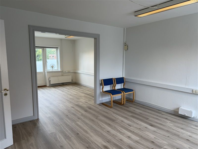 En tom og ren kontorrum med hvide vægge og gulv. To blå stole står mod væggen. En tærskel og dør ligger mod venstre. To