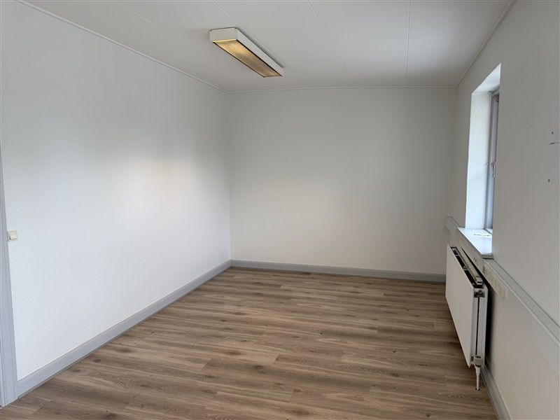 En tom kontorlokal med hvide vægge og gulvtæppe samt vinduesglas og radiator ved væggen
