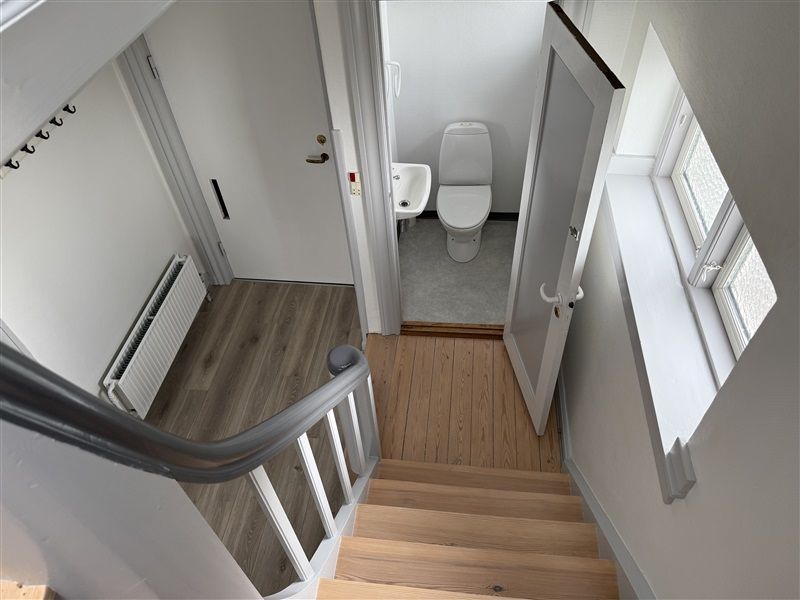 Trapper med lyse trætrin og metalgevær fører til et badeværelse med hvid toilet og hvidt badekar.