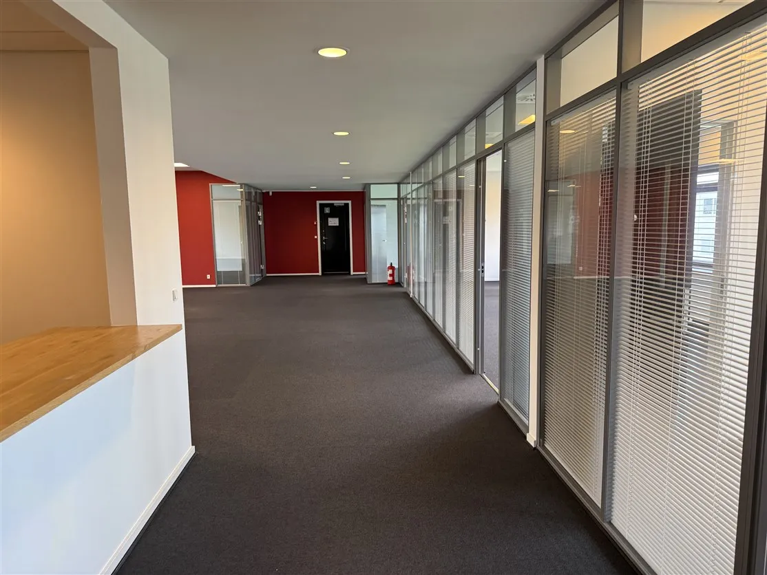 Kontorrum med gulvbelægning, glasvinduer og hvide vægge samt røde og hvide vægge med døre og et ildslukssluk