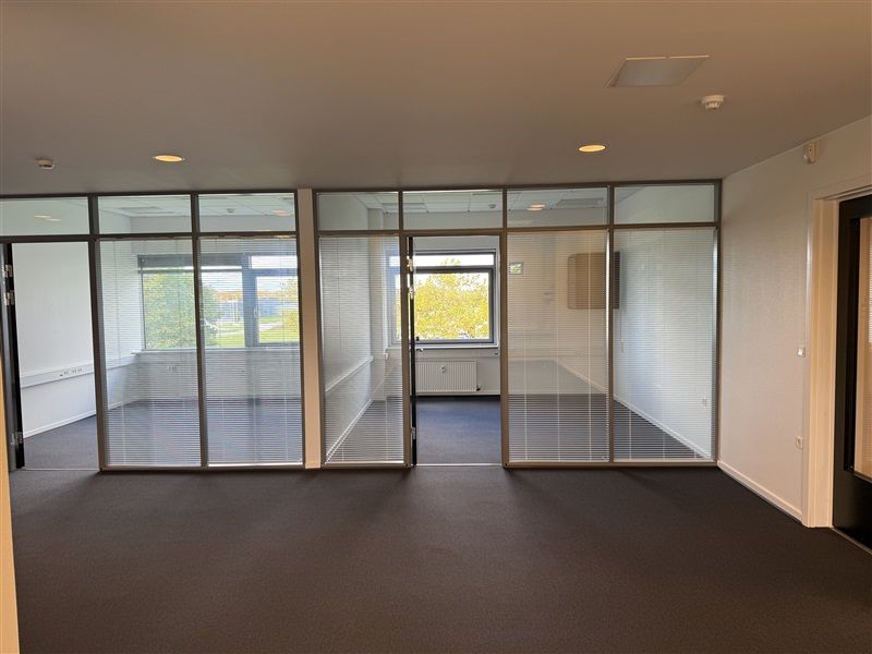 Lokale med glasvinduer og glidedøre, lyse loftslamper og søjler, gulvbelægning og hvide vægge