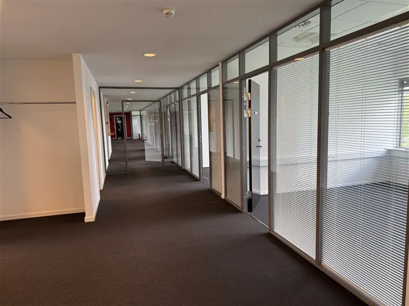 Tomt kontorlokal med hvide vægge, gulvbelægning, glasvinduer, døre og en hængekrog med en tøjstativ