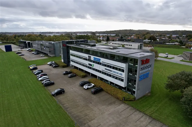 Firmabygning med parkeringsplads og udsigt til byen og vandet i baggrunden med mange solceller på taget