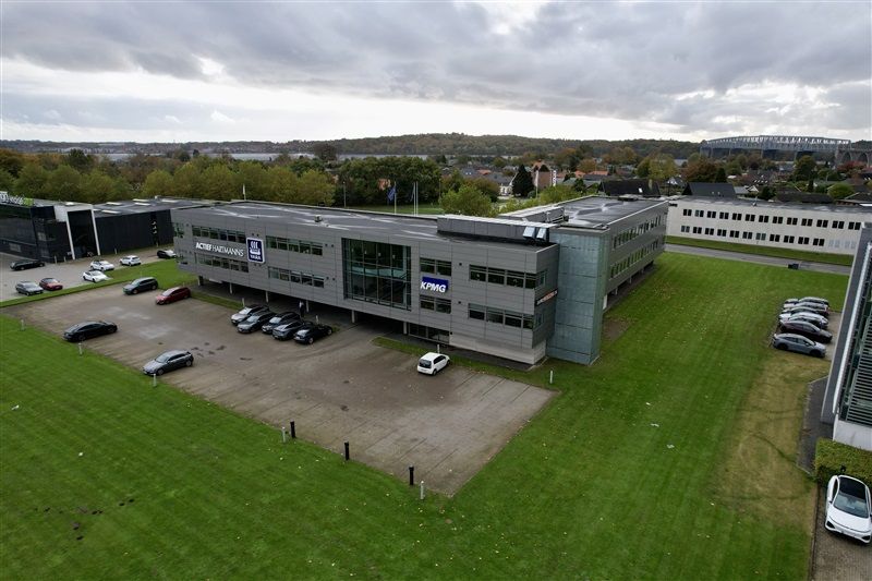 Moderne kontorbygning med parkeringsplads, KPMG logo og biler parkeret på grøn græsplæne