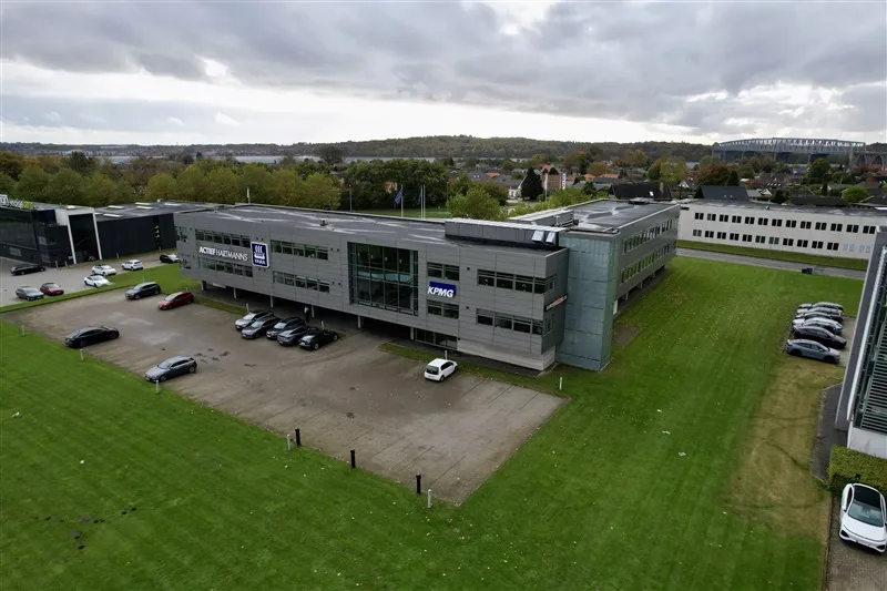 Moderne kontorbygning med parkeringsplads, KPMG logo og biler parkeret på grøn græsplæne