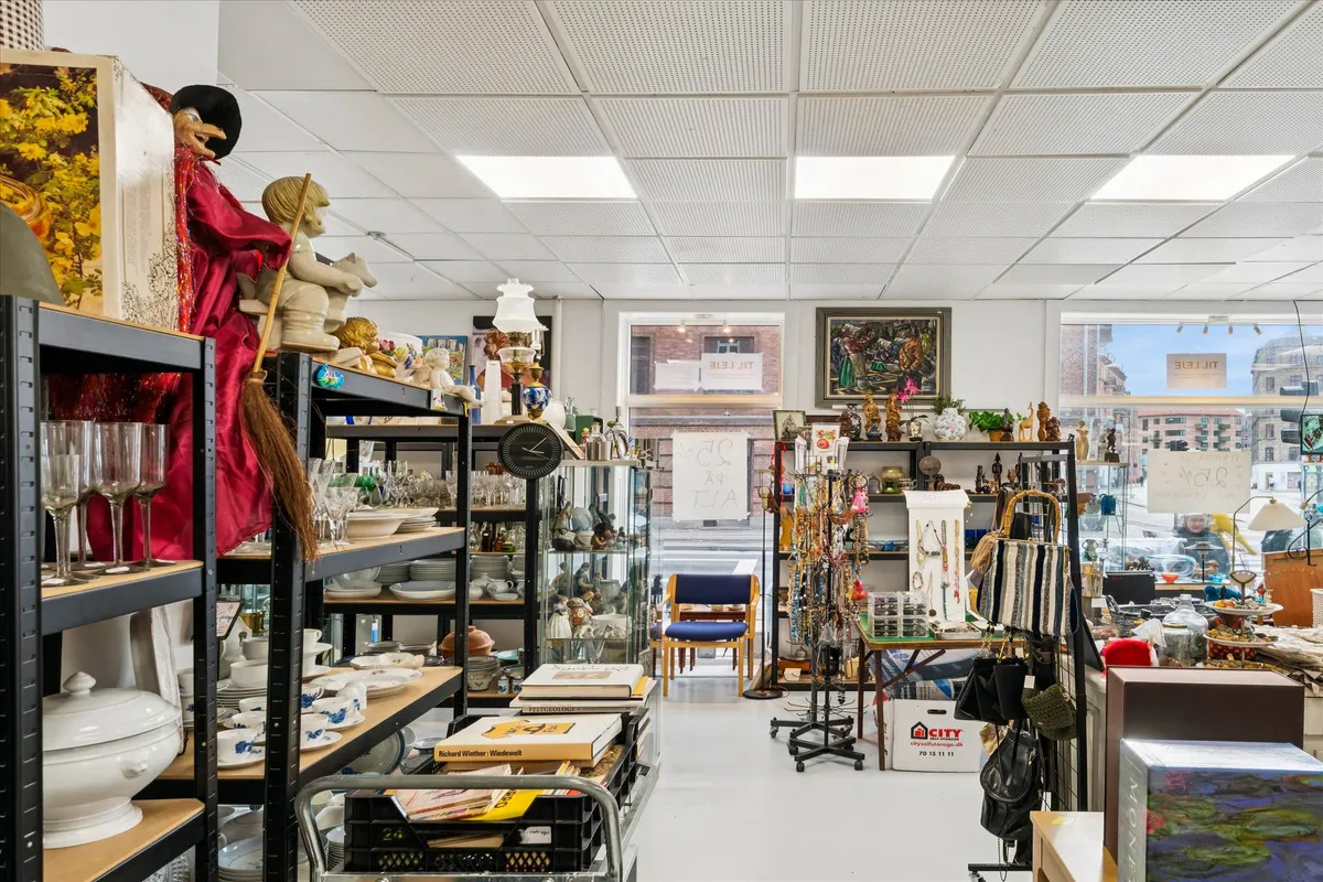 Køkkenborde og tallerkener opbevaret på hylder og skabe i et butiksrum med udstillingsvinduer og kunstværker