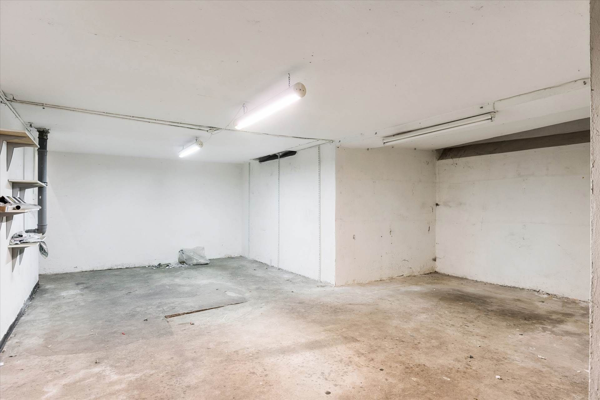 Et ubenyttet lager med hvide vægge og gulv, samt to lysekroner, der er tændt, og en åben dør i midten