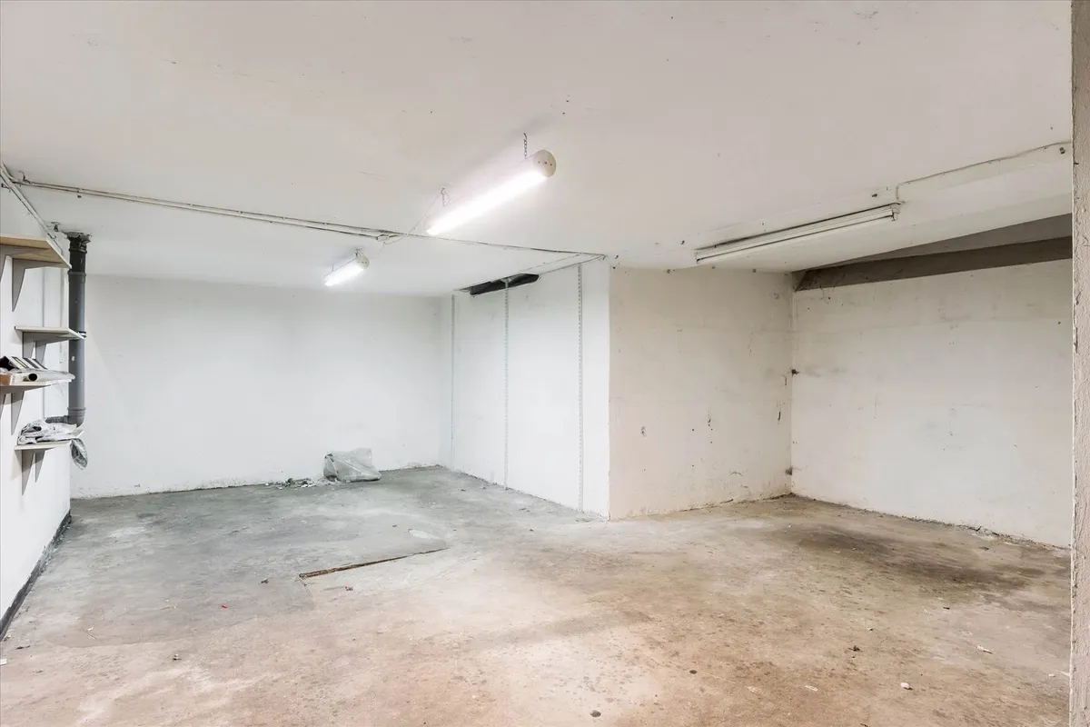 Et ubenyttet lager med hvide vægge og gulv, samt to lysekroner, der er tændt, og en åben dør i midten