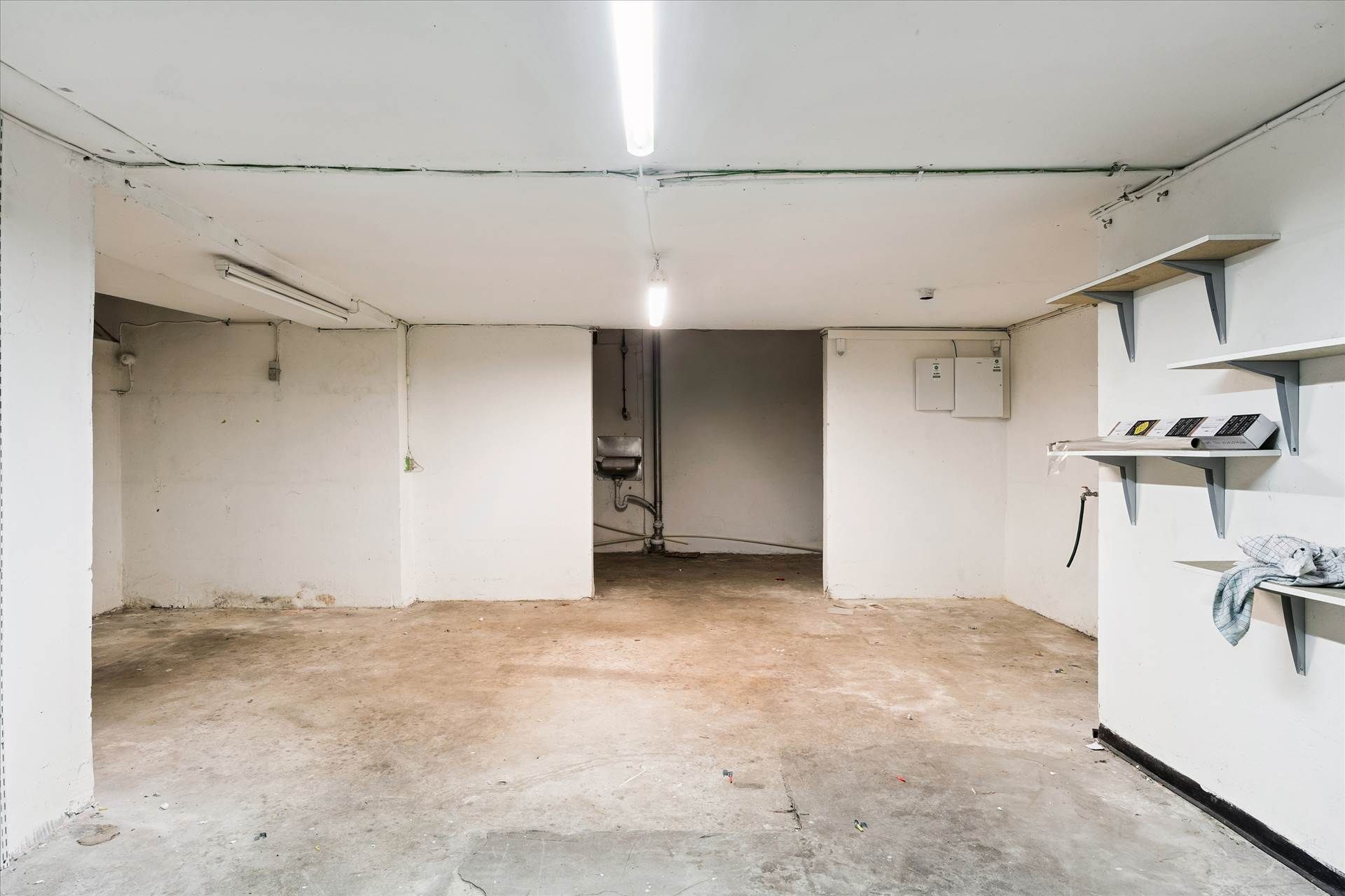 En tom garage med en metalhylde og et skur. Loftet er hvidt og lysekroner er installeret. Der er en åbning i væggen, der