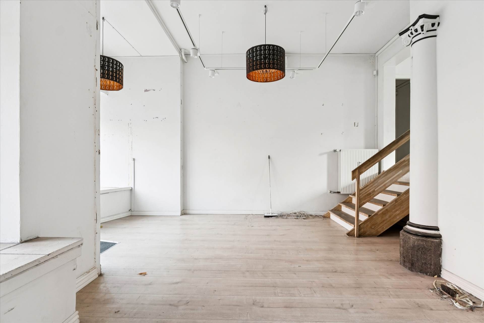 Lyst og indbydende erhvervslejemål med lyse lofter og højde, trætrapper og hvide vægge, dekoreret med lysekroner og trægulve