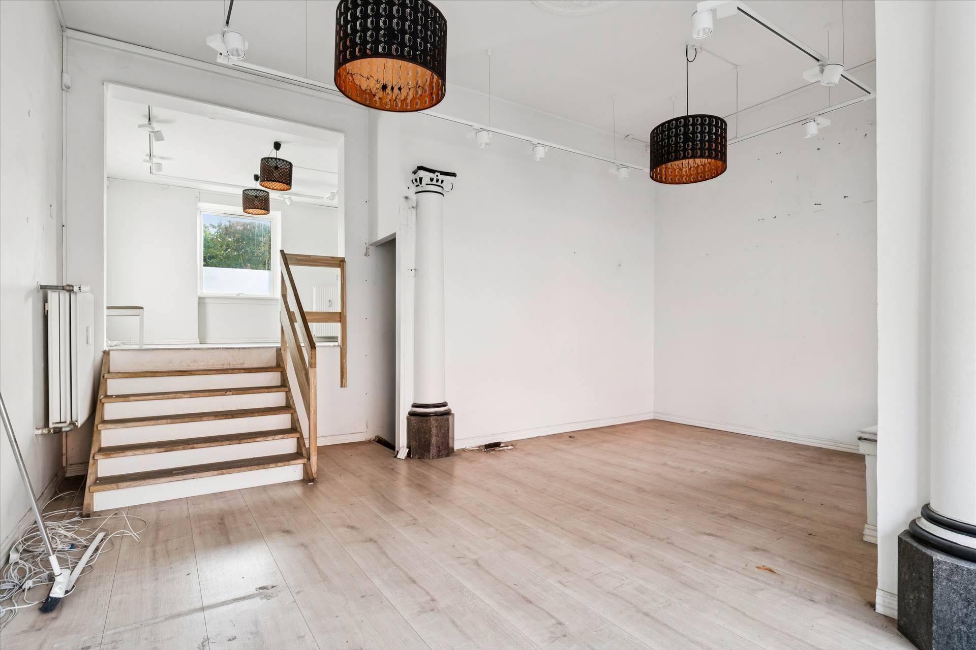 Erhvervslejemål med to etager, hvidt loft, lyse gulve og lysekroner, lyse trætrapper og en slank søjle