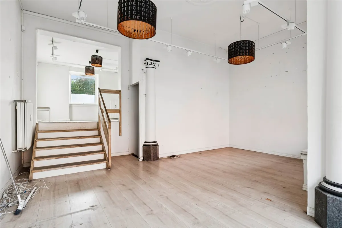 Erhvervslejemål med to etager, hvidt loft, lyse gulve og lysekroner, lyse trætrapper og en slank søjle