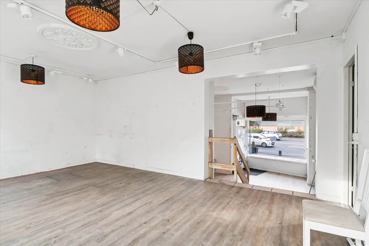 Erhvervslejemål med åbent rum, trægulv og hængelampe, trætrappe og døre til gårdhave