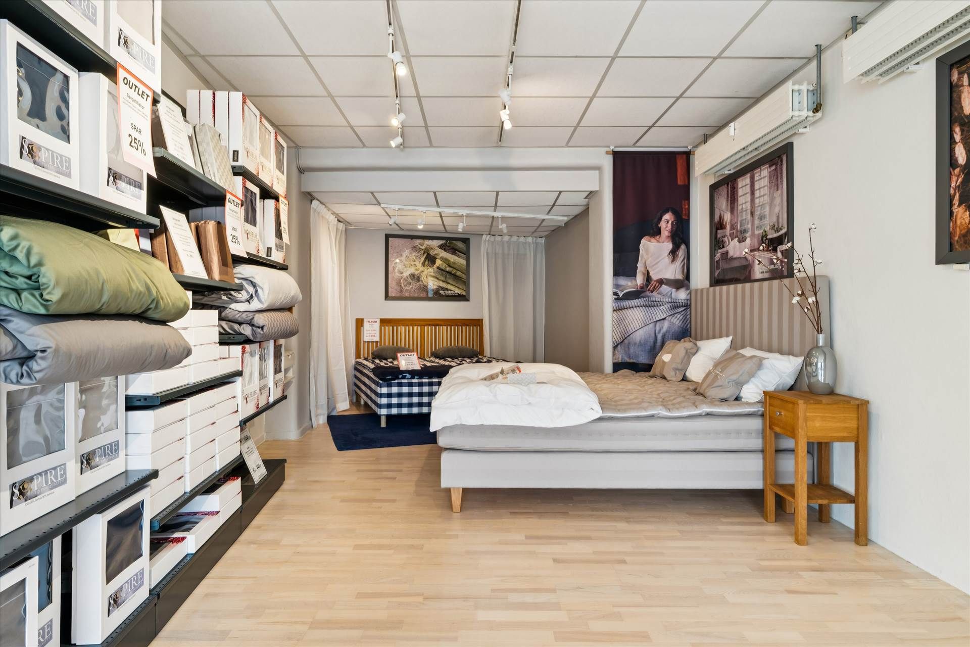 Møbelforretning med møbler, madrasser, tæpper og tøj på hylder og et stort soveværelse med trægulv og hvidt loft