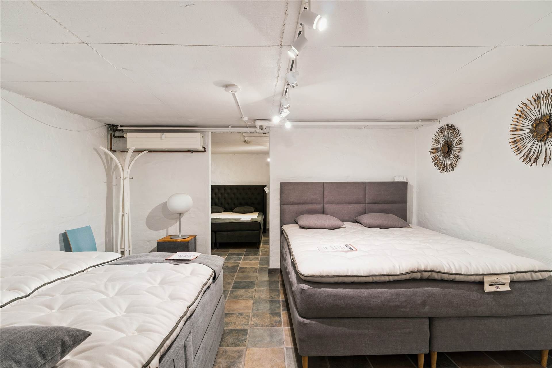 Et showroom med to nye sengebøffer og to ekstra sengebøffer med togæsser og hovedpuder i den bageste del af showroommet