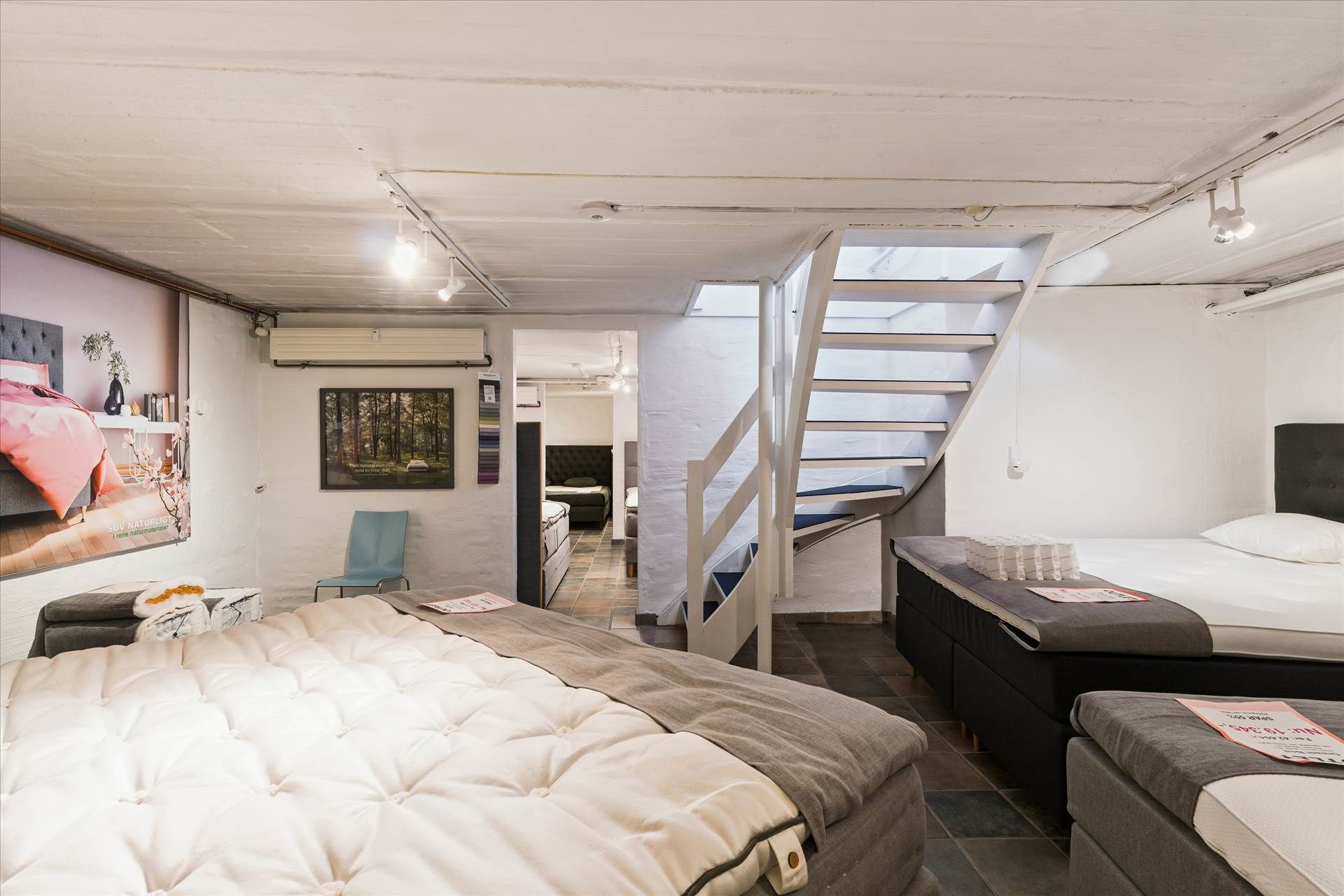 Et moderne og stilrent møbelforretning med tre senge og loftstrapper i hvidt og gråt. Lejemålet med 349 m² og store vinduer