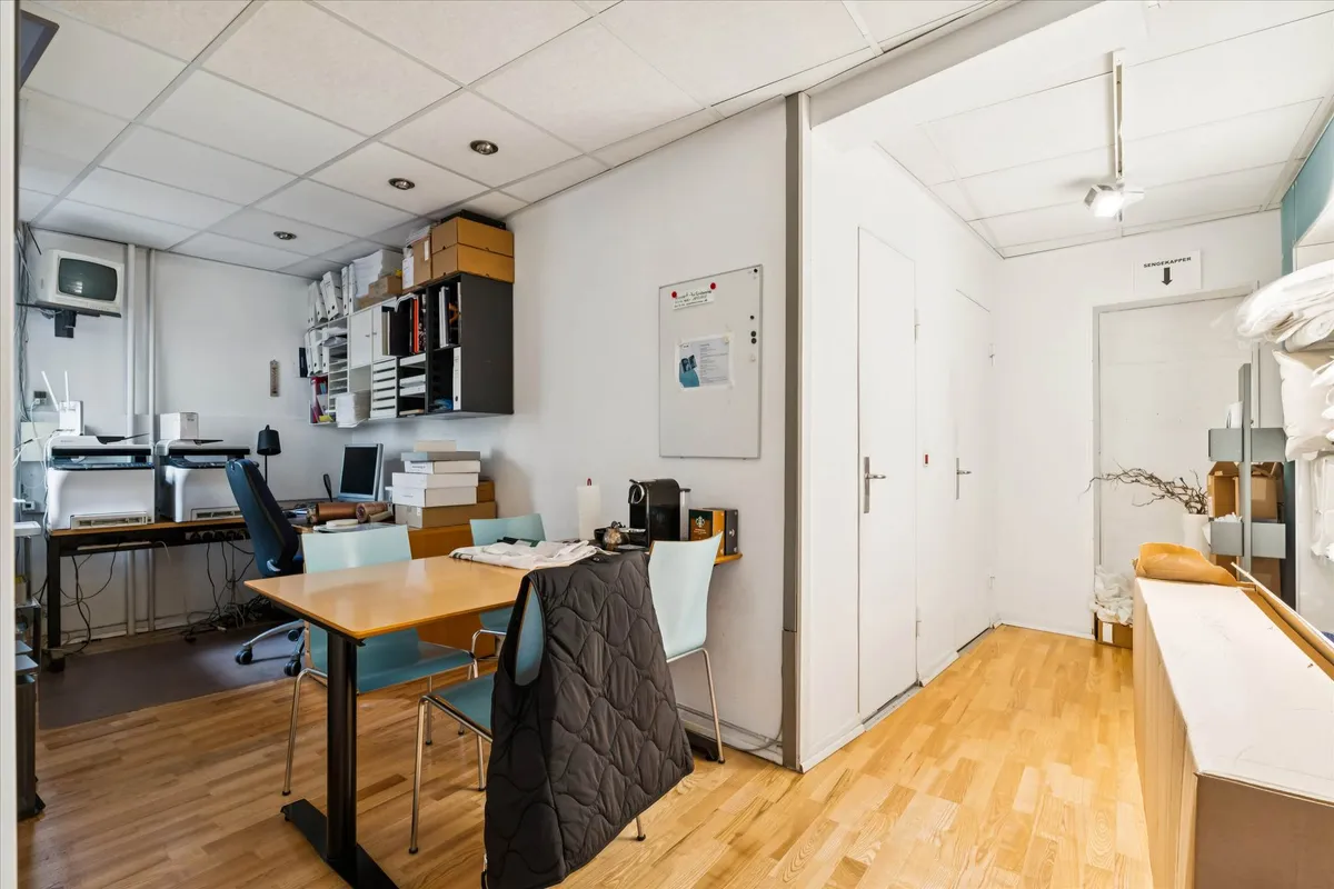 Erhvervslejemål med skrivebord, kontorstoles, printer og sengekasser i lyse farver på gulvet og væggene