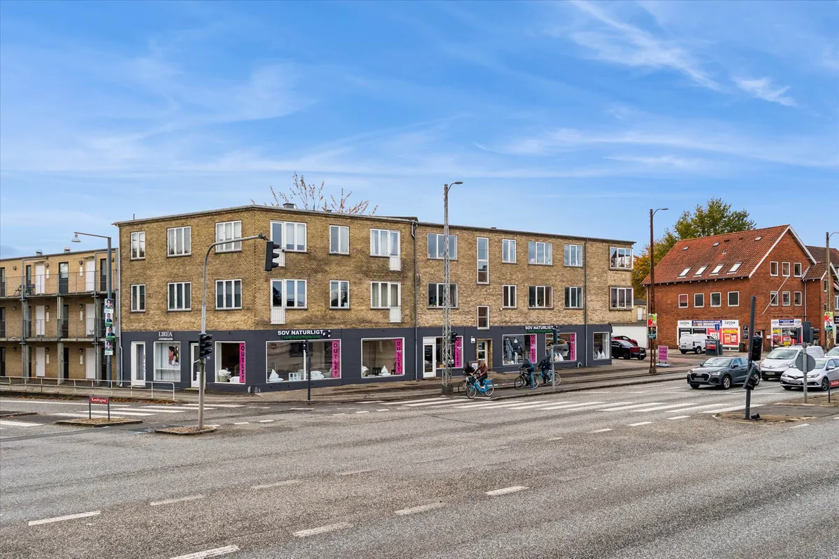 Et moderne erhvervslejemål med udvalgte butikker og et parkeringsområde i baggrunden, hvor cyklister krydser gaden