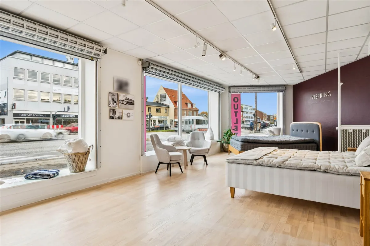 En moderne indretning med møbler og tekstiler samt en stor facade mod en trafikeret vej.