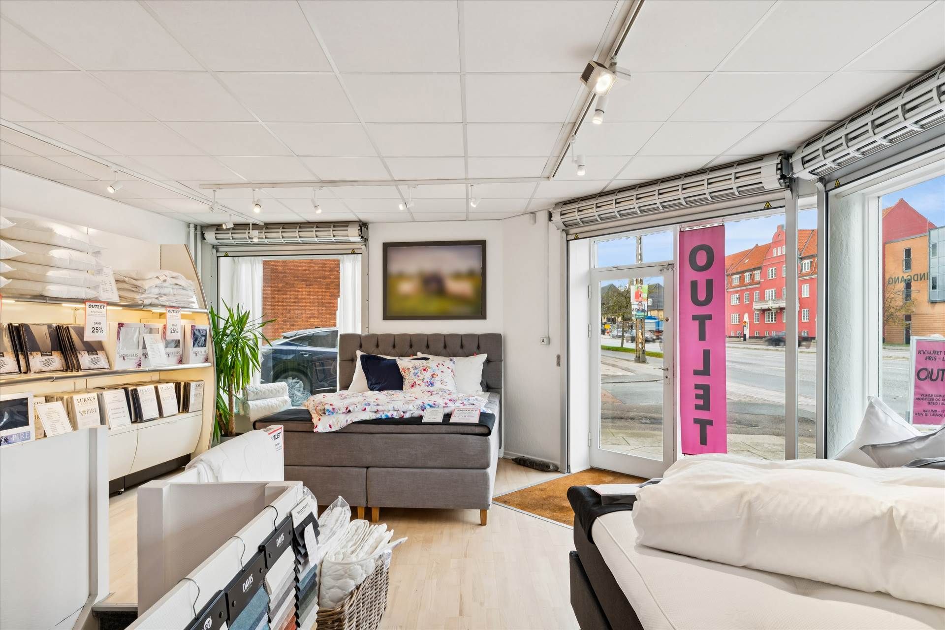 Lejemålet med store vinduer og en pink skilt med teksten Outlet. Inde er der senge med tæpper og pude, samt nogle tæpper og