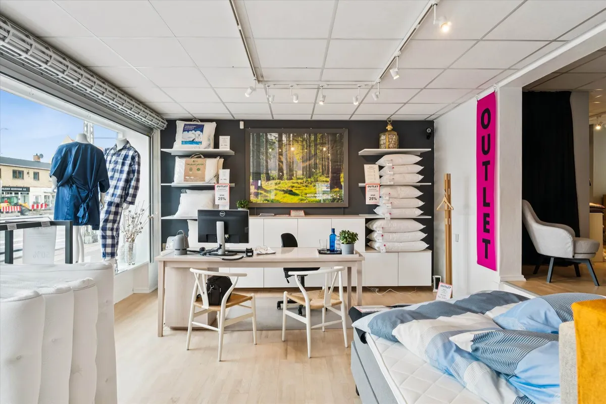 En stue med to stole, en skrivebord og en sofa med tøj. En væg er dækket af hyggeligt tøj og et sæt puder.