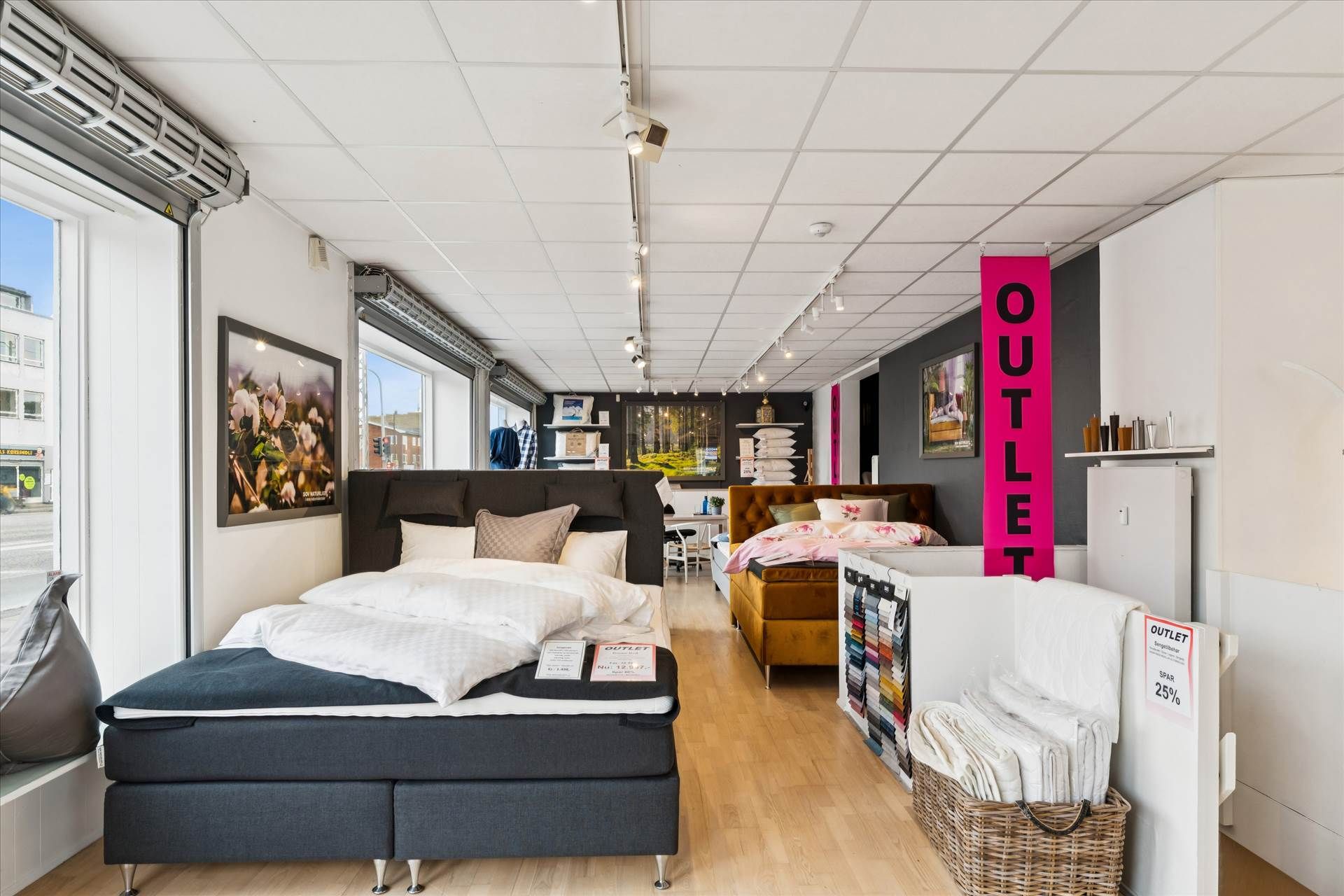 Interiør i møbelforretning med store senge, pyntede med puder, og udstilling af tæpper og andre tekstiler.