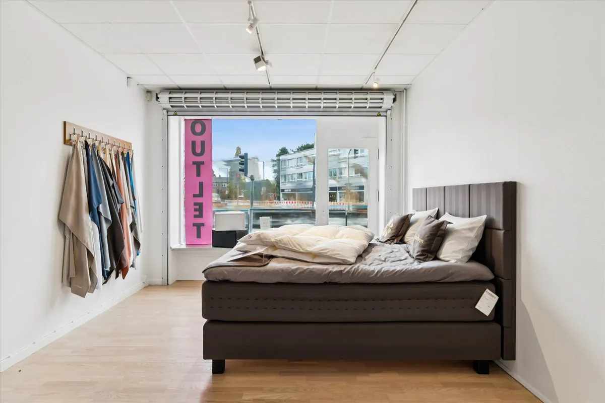 Erhvervslejemål med stor facade mod Roskildevej, rummelig soveværelse med senge og tøj og udsigt til gaden med grønne træer