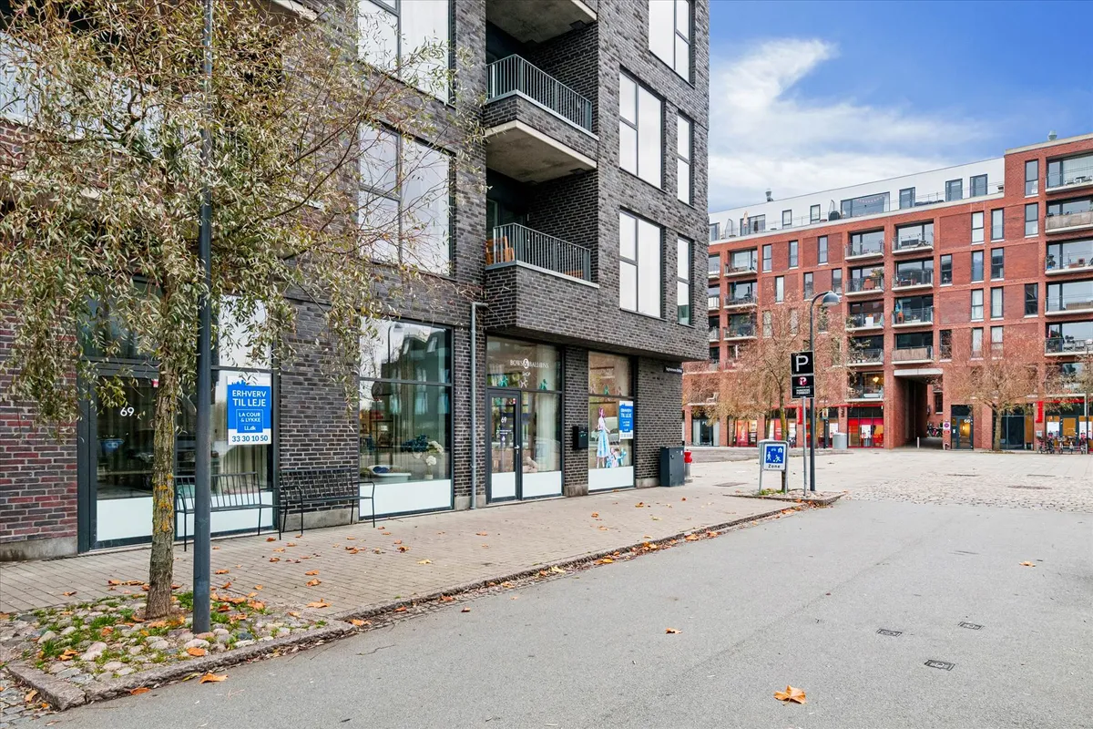 Moderne butik med glasvinduer og terrasse på Teglholmens Østkaj. Tegn på leje og åbningstider. Solrig dag med spredte skyer.