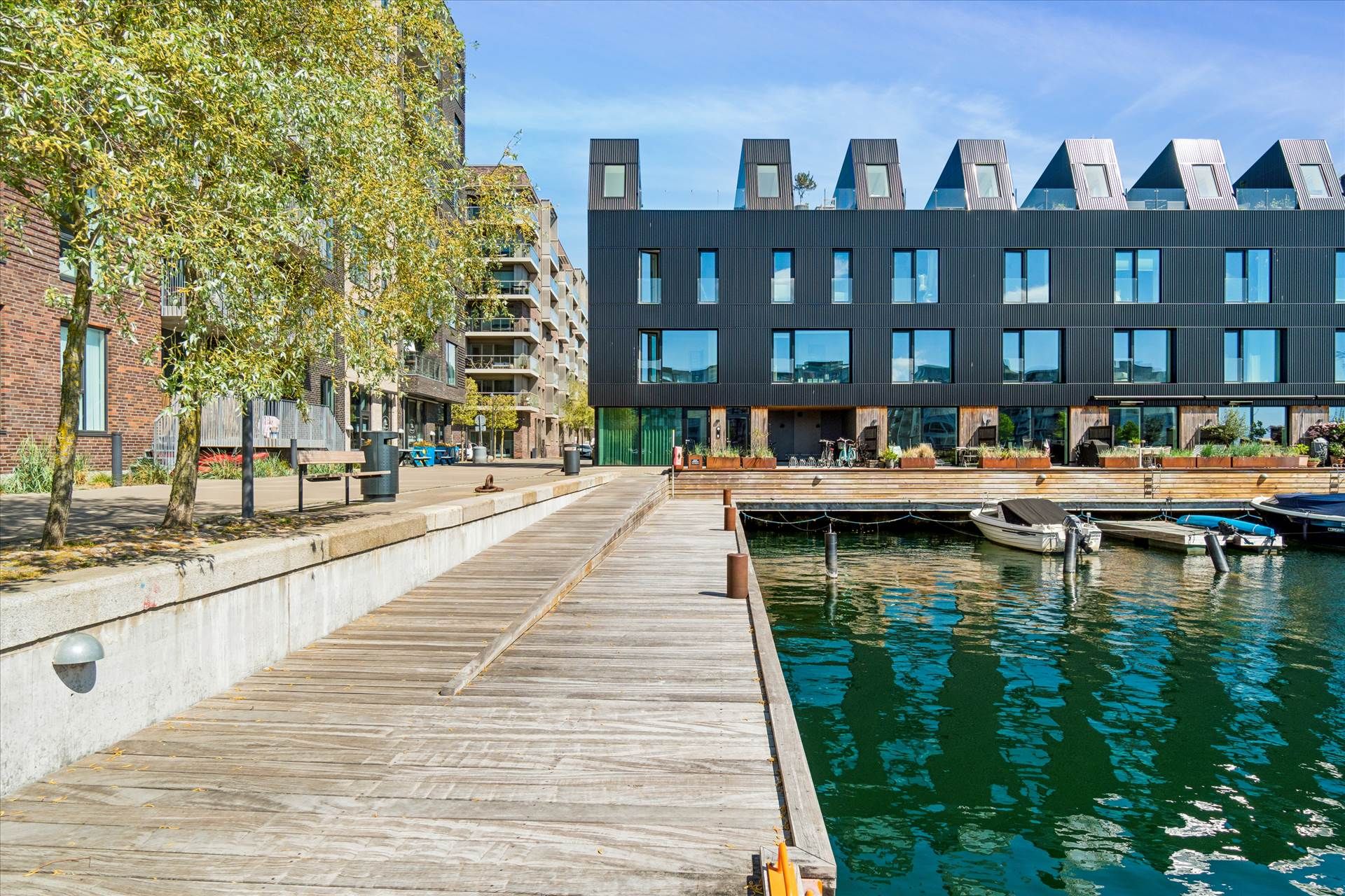Butikslokale med vandudsigt på Teglholmens Østkaj, træbro, parkerede både og moderne bygning med glasvinduer og tegltag
