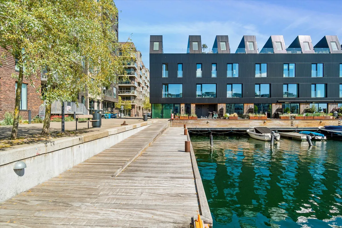 Butikslokale med vandudsigt på Teglholmens Østkaj, træbro, parkerede både og moderne bygning med glasvinduer og tegltag
