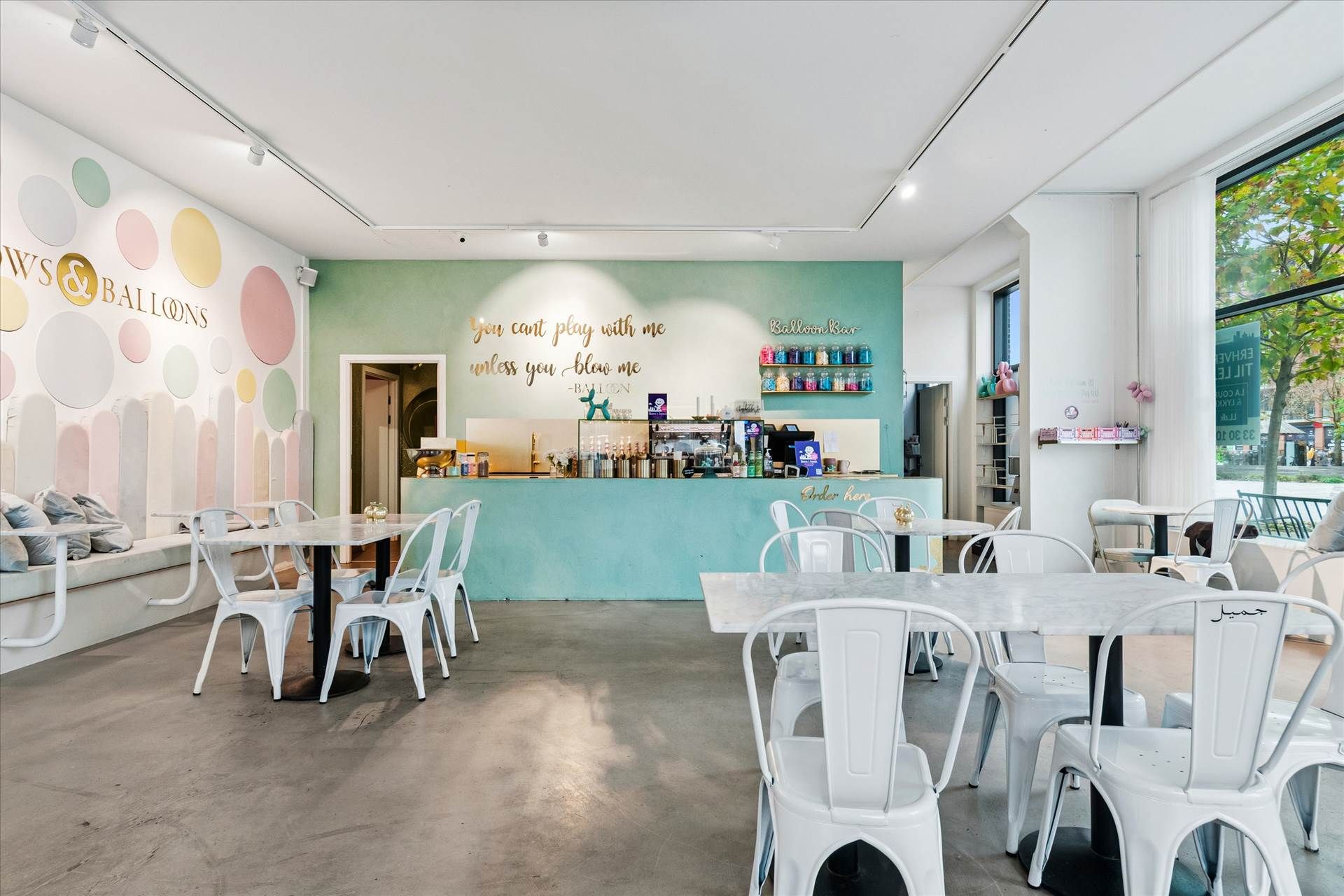 Inde i en restaurant med hvide stole og runde borde, der vender mod en køkkenbar med en skriftlig indskrift, som siger "You