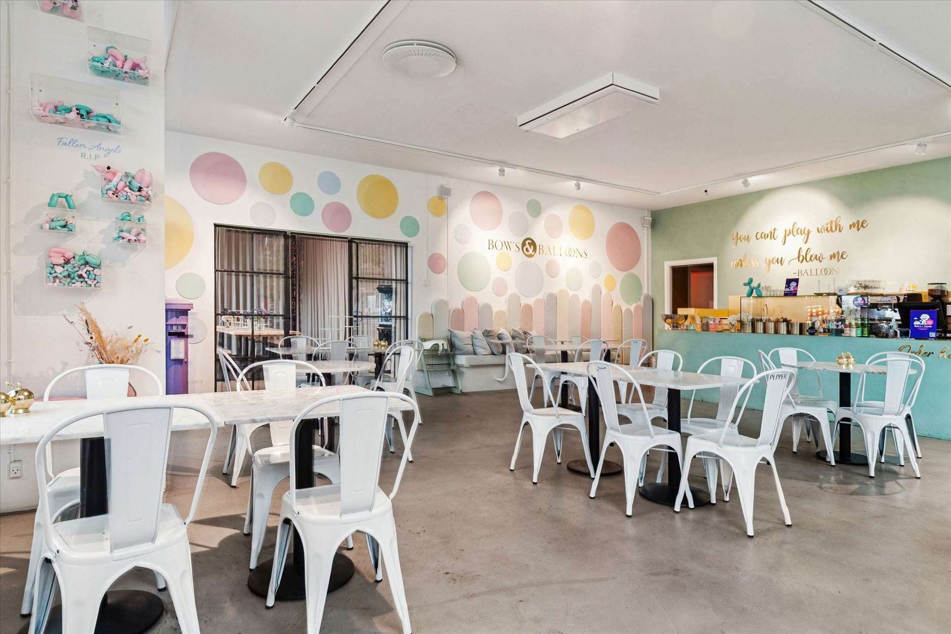 Højt loft med luftkanaler, vægge med mønstre, hvide stole, runde borde, skrivebord, sofaer, kaffemaskine, skærme,