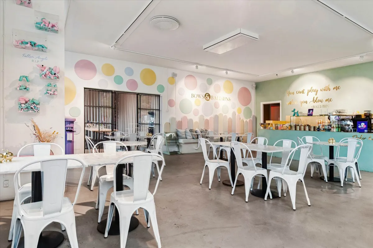 Højt loft med luftkanaler, vægge med mønstre, hvide stole, runde borde, skrivebord, sofaer, kaffemaskine, skærme,