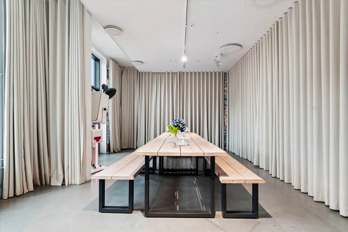 En stor træbord med to bænke og en vase med blå blomster står i et rum med hvide væggardøjer og loftsventilatorer