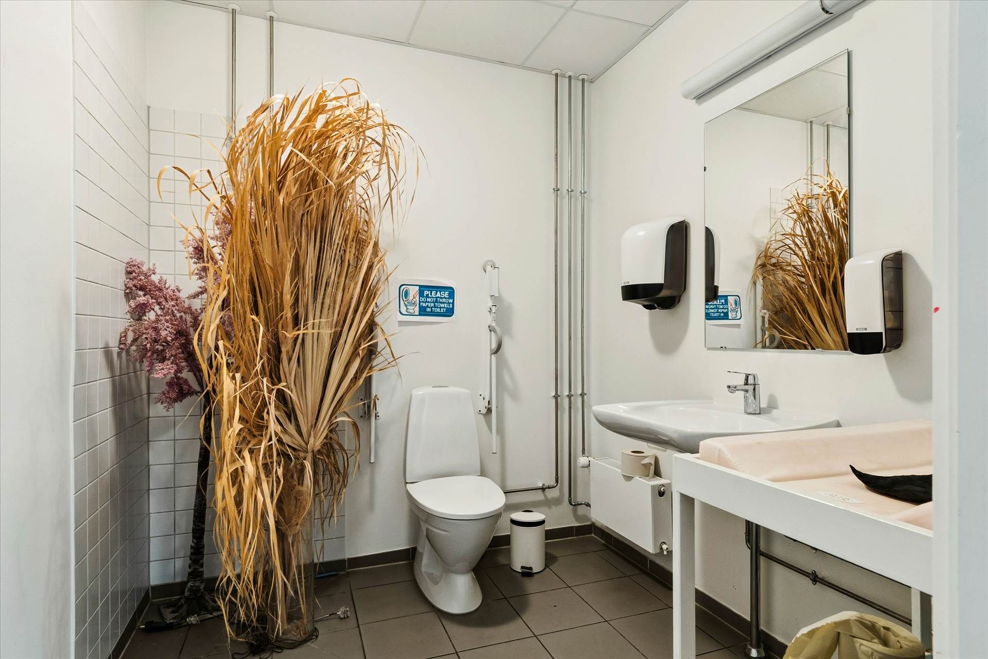 Moderne toiletrum med hvidt toilet, dobbeltvask og to hængede hånddesinfektionsflasker i et rent og velplejet lokale