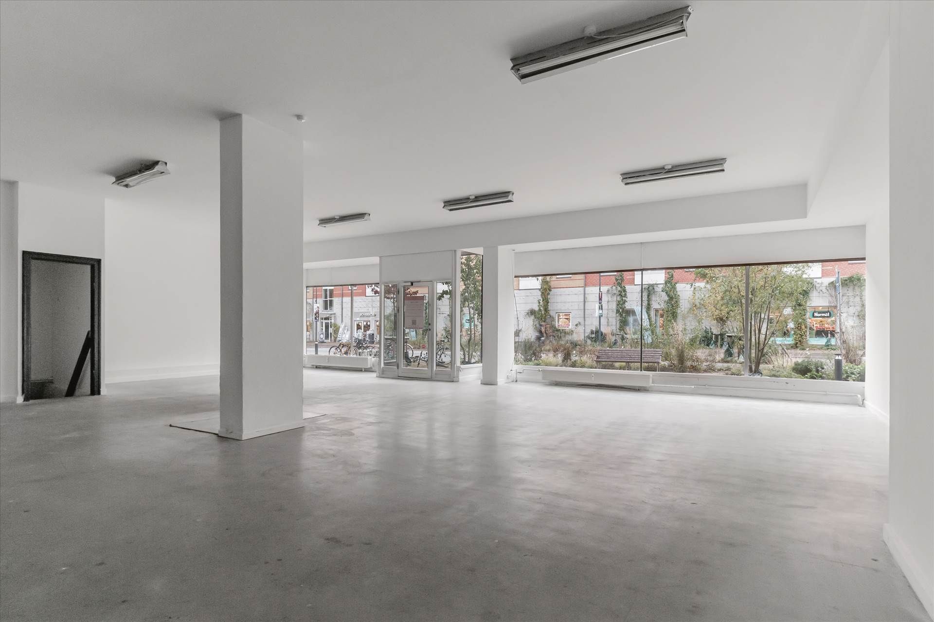 Store glasruder med træbænke og planter udenfor og lyse og hvide vægge inde med højt til loftet