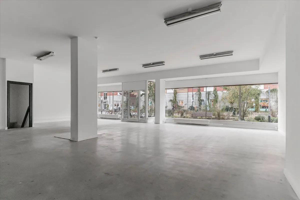 Store glasruder med træbænke og planter udenfor og lyse og hvide vægge inde med højt til loftet