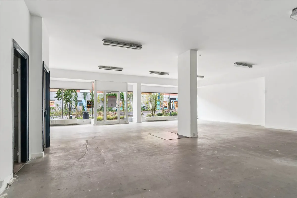 En stor og ren butik med hvide vægge og gulv, flere lysekroner og vinduer med udsigt til gaden