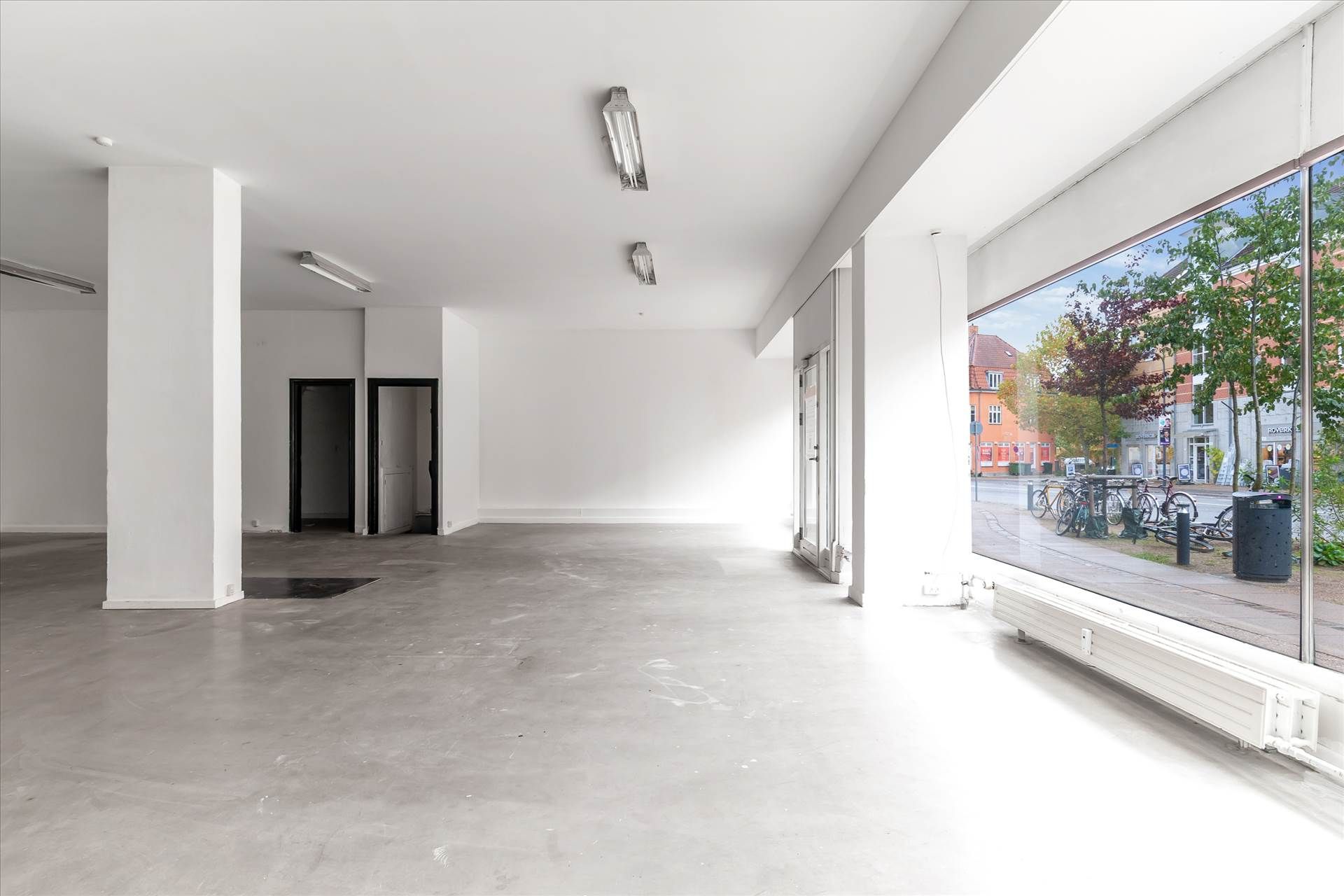 Moderne, ubenyttet butik med højt loft og store ruder, der giver masser af lys og en flot udsigt til gaden med planter og