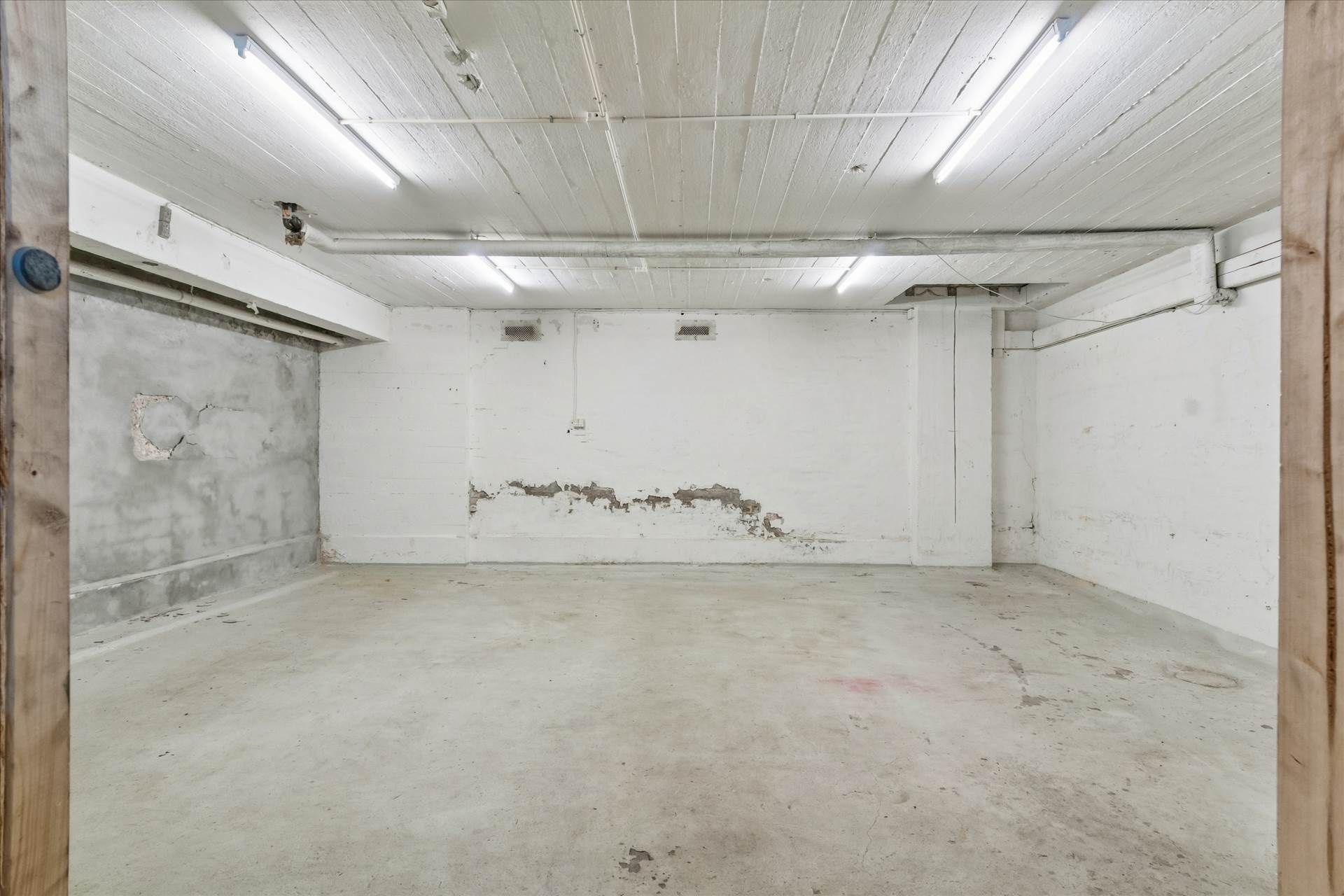 En tom og ren garage med hvide vægge og gulv samt hvide lofter med to lange lyse.