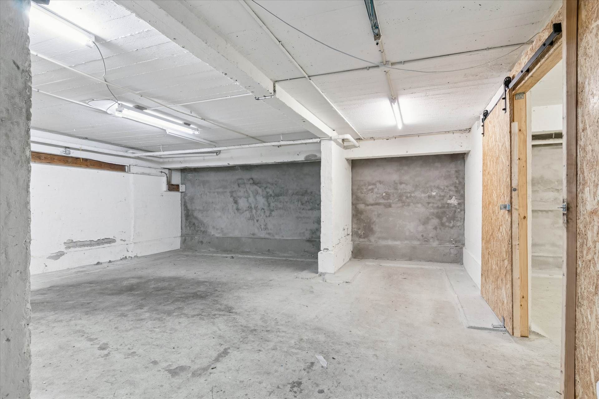 En stor og nyrenoveret kælder med to store parkeringspladser, hvor gulvet er hvidt og væggene er cement og hvidt