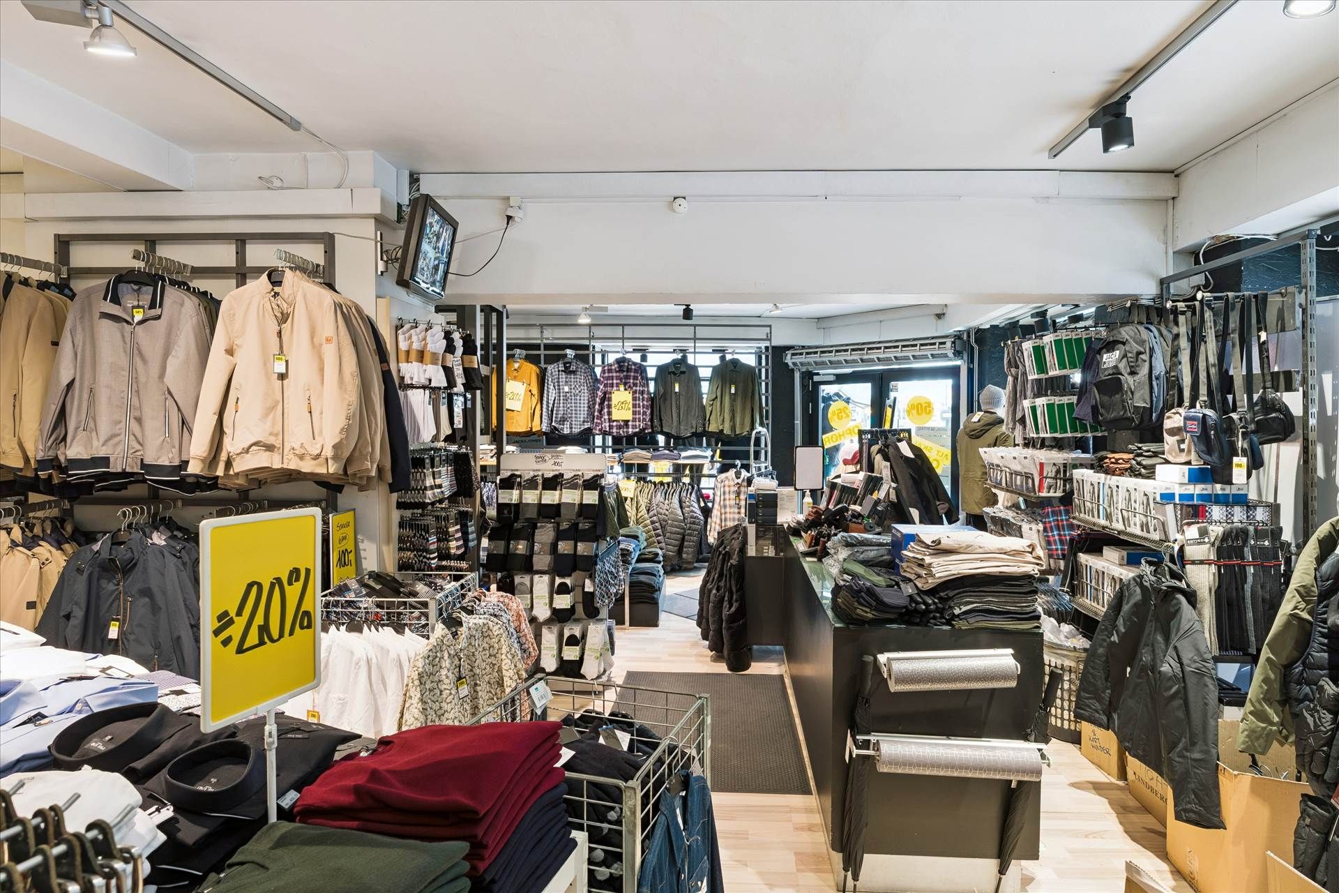 En stor butik med tøj og jakkestativer, indretning med moderne design og tavle med rabat 40% og tv-skærm på væggen